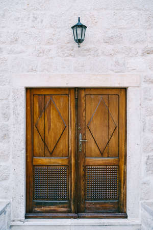 Wooden brown doors with carved elements and patterns in a white wall with a lantern.の写真素材