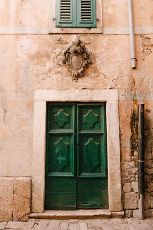 Closed double-leaf green wooden doors with patterns under the window and a carved figure in the wall.の写真素材