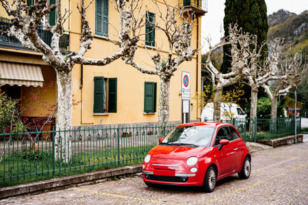 Milan, Italy - 29 july 2020: A red Fiat 500 car parked outside a house with sycamore trees, or chinar in the garden, in Varena, Italy.のeditorial素材