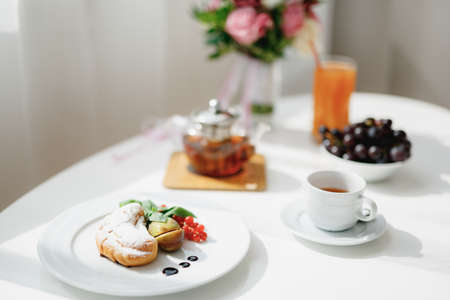 Close-up of a plate with a croissant, sliced figs and a sprig of red currants on a white table.の写真素材