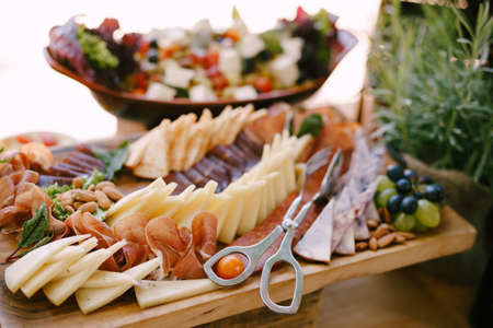 Close-up of a wooden cutting board with meat and cheese cuts and a grape cube on the background of a...