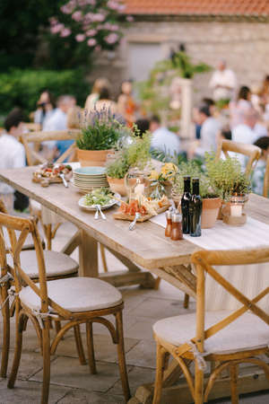 A festive table with fresh flowers in pots in a restaurant with chairs and guests on a blurred...