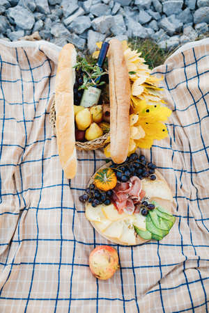 Food for a picnic in nature on a fabric bed with a baguette, a bottle of wine, fruit and cheese and cold cuts.の写真素材