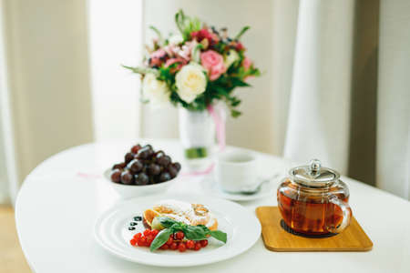 Elegant table with a bouquet of flowers, a plate with a croissant, tea and grapes.の写真素材