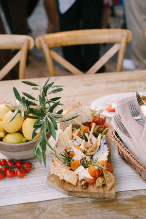 Cutting board with cheeses, pickles and figs on the table with a plate of lemons and cherry...