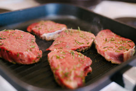 Four raw steaks are fried on a grilled pan.