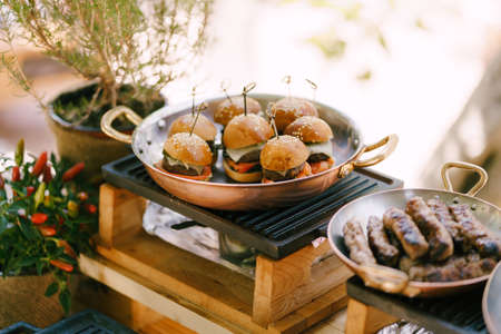 Mini burgers on a large copper frying pan with Serbian cheapchichi sausages and a bush of bitter pepper in a pot.の写真素材
