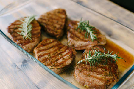 Beautiful toasted steaks in a glass plate on a wooden background, in their own juice and sprigs of rosemary.の写真素材