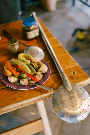 A large spoon for stirring pilaf. A plate of hot pepper and garlic on the table.の写真素材
