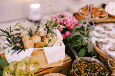 Wooden box with bread rolls on the background of oysters, stuffed olives and a bouquet of flowers.の写真素材