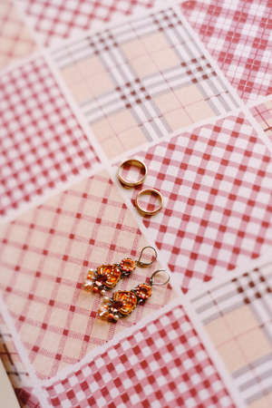 Golden wedding rings. Earrings with stones and gold wedding rings on checkered fabric.の写真素材