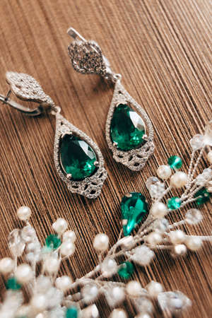 Close-up of earrings with a large green stone and a decoration of white beads on a brown background.の写真素材