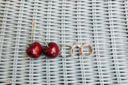 Three golden rings with two ripe red cherries on a grooved surface.の写真素材