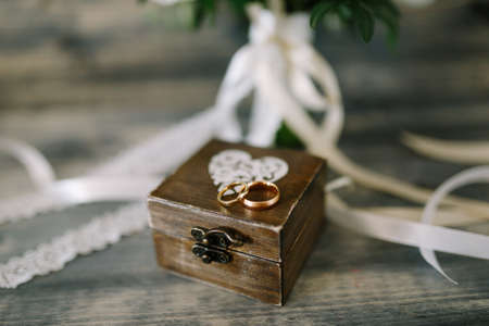 Closed wooden box with a heart and gold rings for the bride and groom on a background of white ribbons.の写真素材