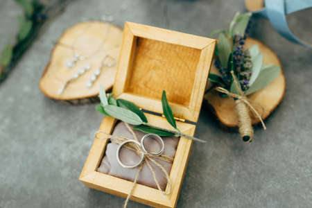 An open wooden box with wedding rings and wooden stands with jewelry and a bouquet of flowers.