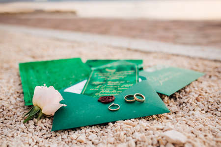 Gold wedding rings for the bride and groom on a green envelope with invitations on decorative...