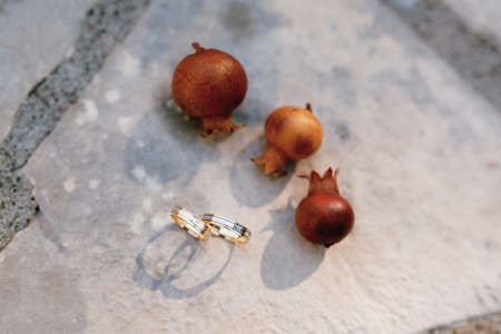 Wedding rings of the bride and groom on a stone texture with small pomegranate fruits.