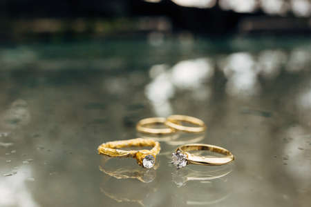 Gold wedding rings, an engagement ring and a foil ring on a blurred background with water drops.