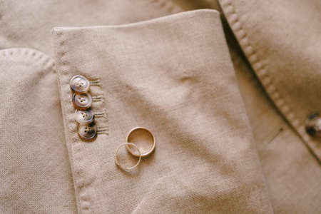 Two gold wedding rings on the sleeve of a beige mens jacket with buttons.の写真素材