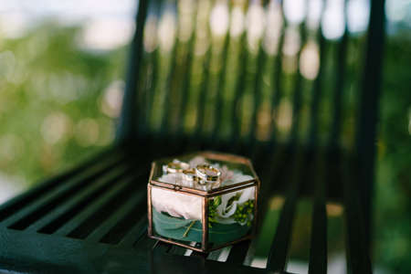 An engagement ring and wedding rings made of gold on a decorative glass box with a pink flower on a...