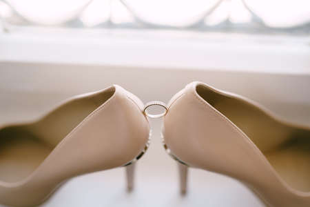 Wedding ring of the bride on a white background with the brides shoes in beige.の写真素材