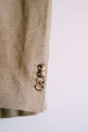 Close-up of buttons on the sleeve of a mans beige jacket on a white background.