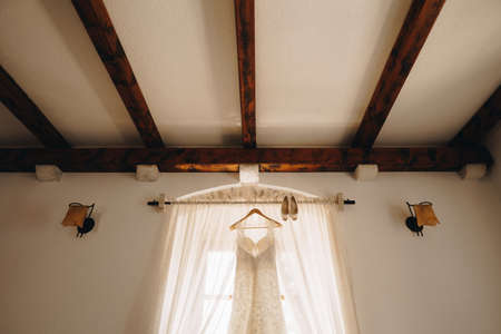 A bright room with a wedding dress on a hanger on the cornice and the brides shoes.の写真素材