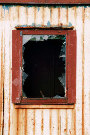 Window opening with broken glass in a rusty metal wall.