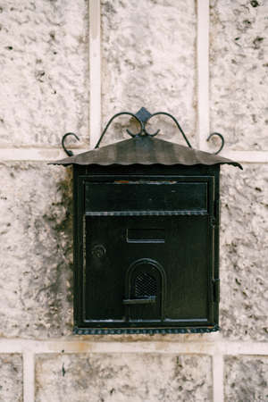 Close-up of a black metal mailbox on a stone wall.