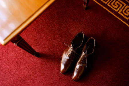 Brown mens shoes with laces on a red carpet in a room by a wooden table.の写真素材