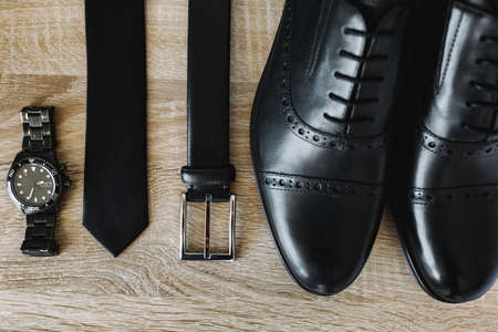 New mens shoes, belt, tie and wristwatch in black on a wooden texture.の写真素材