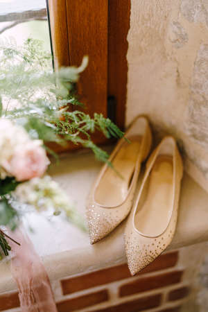 A window sill by a wooden window with a bouquet of flowers and ballet shoes with small shiny pebbles.の写真素材