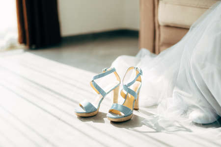 Blue high-heeled bridesmaid shoes on the floor by the train of the wedding dress in the room.の写真素材