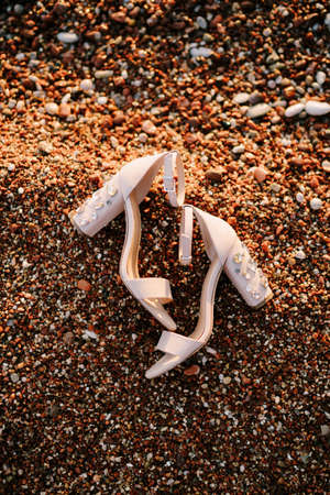 Bridal sandals with thick heels adorned with jewelry stones on a pebble beachの写真素材