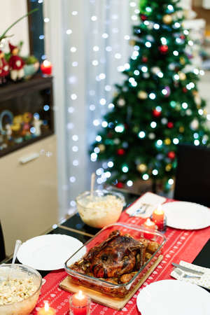 Close-up of a Christmas duck on a festive table, against the background of lights of garlands on a Christmas tree. Poultry baked until crispy with potatoes and apples in its own fat.の写真素材