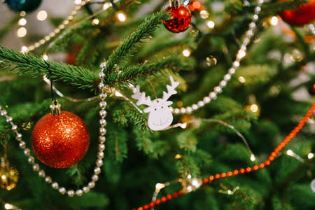 A wooden toy in the shape of a deer head on the branches of a Christmas tree, surrounded by beads,...