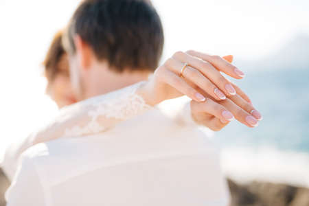 bride and groom are hugging on the rocky beach of the Mamula island, the bride put her hands on the grooms shouldersの写真素材