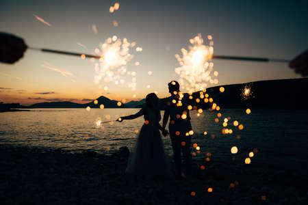 the bride and the groom standing on the on the beach of the Mamula island and holding sparklers at the sunsetの写真素材