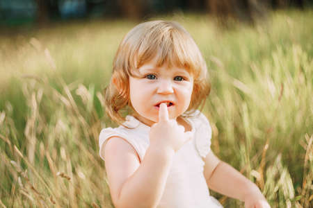 little girl sits outdoors and holds a finger in his mouth