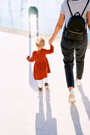 Mother and daughter walking hand in hand by the sea on a sunny day