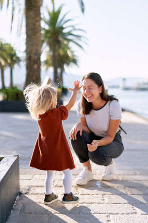 2-year old girl is splashing water from the fountain on her mother on a boat pierの写真素材