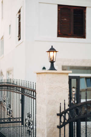 Included street lamp in black on a column of a metal fence near a white building.