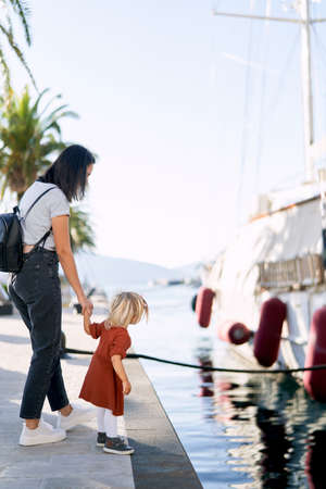 Mother and daughter are looking at a boat in a marina on a suuny day
