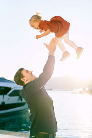 Father is throwing his 2-year old daughter in the air at sunsetの写真素材