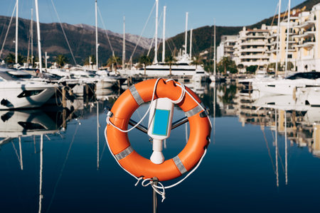 A close-up of a lifebuoy on a stand on the dock overlooking the mountains and yachts on the water. Marina for yachts in Montenegro, in Tivat, near Porto Montenegro.の素材 [FY310162393426]