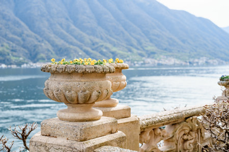 An architectural flowerpot on a stone fence against the backdrop of water and mountains.の写真素材