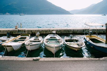 Close-up of fishing boats at the pier of the city of Perast against the backdrop of mountains and blue sky.の写真素材