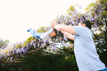 6-year old is flying in his dads arms under a wysteria treeの写真素材