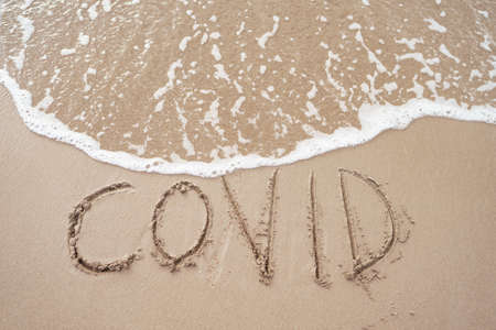 COVID lettering on a sandy beach with a foamy sea wave.の写真素材