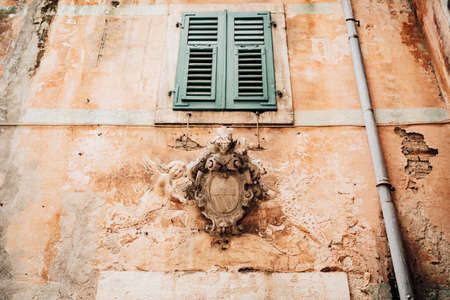 An old shabby building with a closed window and a bas-relief under it in the old town of Kotor in...